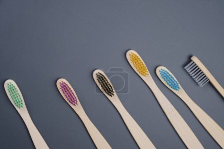 Five toothbrushes are neatly lined up in a row on a wooden table, creating a symmetrical arrangement. The toothbrushes vary in color and size.