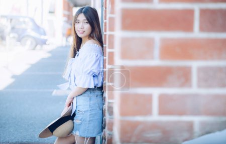 Foto de Retrato de mujer asiática joven apoyada en la pared de ladrillo y mirando a la cámara. - Imagen libre de derechos