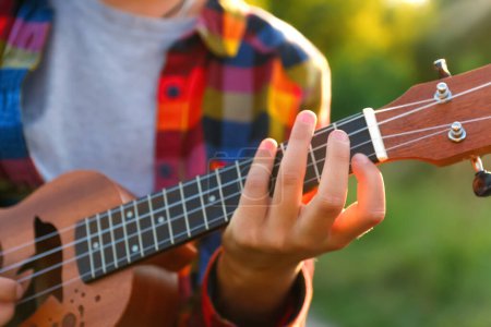 Foto de Desenfocar a la mujer está aprendiendo a tocar el ukelele. Girl sintoniza una guitarra en miniatura antes de un concierto. Afuera. Fuera de foco. - Imagen libre de derechos
