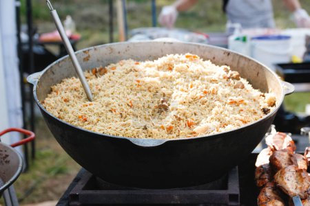 Photo for Defocus stirring the pilaf in a large bowl during cooking outdoors. National dish. Cooking of traditional pilaf in big cauldron, street food in outdoor. Festival. Out of focus. - Royalty Free Image