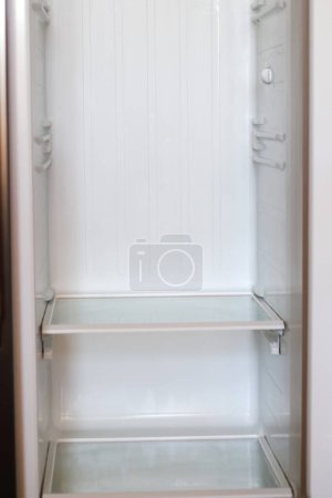 Photo for Empty open fridge with shelves, refrigerator. Inside of an empty white fridge. Vertical. Closeup. Out of focus. - Royalty Free Image