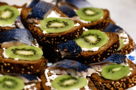 Photo for A delectable sandwich with herring and kiwi fruit on a slice of black bread. Enjoy this healthy treat with fresh herring fish on a dark background. Out of focus. - Royalty Free Image