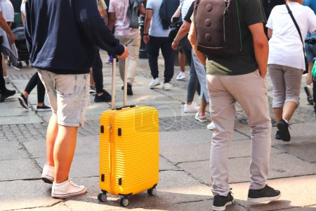 Téléchargez les photos : Homme marchant dans une rue animée avec une valise jaune distinctive, véhiculant l'idée de voyage et de mouvement dans un environnement métropolitain, idéal pour les agences de voyages qui promeuvent les escapades en ville. - en image libre de droit
