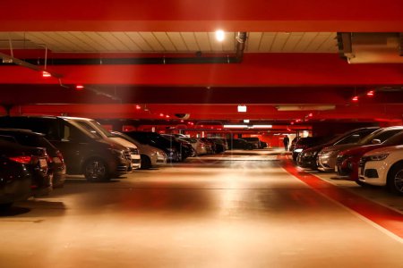 Garaje subterráneo con coches aparcados e iluminados por luces rojas, adecuado para ilustrar medidas de seguridad durante emergencias o para promover aparcamientos seguros. Borrosa..
