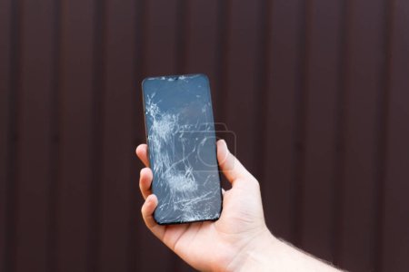 Foto de Smartphone pantalla de cristal roto en la mano sobre fondo marrón. Necesidad de reparación y fragilidad de los dispositivos móviles. - Imagen libre de derechos