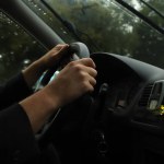 Hand holding steering wheel while driving in the rain. Journey on the road with speed in a rainy day. Person's hands holding a steering wheel in heavy rain, car driver in downpour.