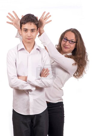Retrato de colegiales lindos. Una chica y un chico con ropa de escuela se están divirtiendo y bromeando, haciéndose trucos el uno al otro. La chica muestra los cuernos.