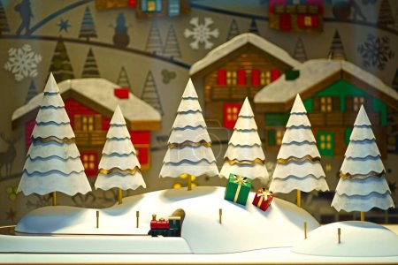 A whimsical window display featuring paper snowy trees and wrapped gift boxes, creating a charming winter wonderland scene