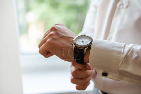 Téléchargez les photos : Un homme en chemise blanche attache le bracelet d'une montre chère sur sa main - en image libre de droit