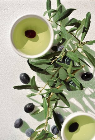 Foto de Plato de cerca con aceite de oliva decorado con hojas de olivo y aceitunas, vista superior - Imagen libre de derechos