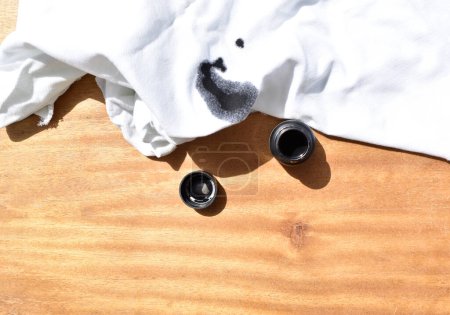 Foto de Vista superior de mancha negra sobre tela blanca con botella de tinta sobre mesa de madera - Imagen libre de derechos