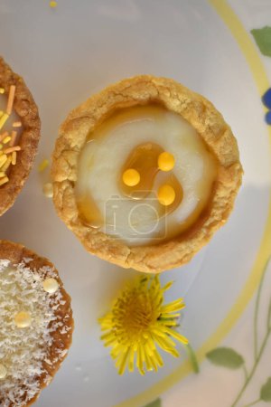 Photo for Mini tarts filled with buttercream on a  beautiful plate decorated by dandelion flower, top view - Royalty Free Image