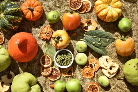 Téléchargez les photos : Nature morte d'automne avec différentes citrouilles, poires, figues, graines de citrouille, pommes vertes, feuilles et kaki sur fond de toile de jute - en image libre de droit