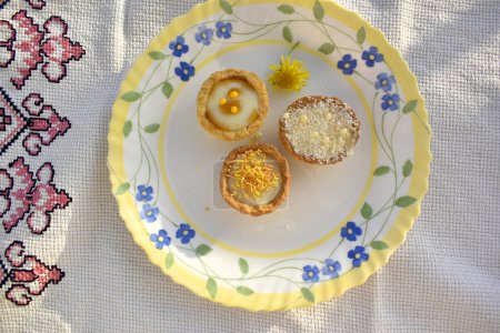 Mini tarts filled with buttercream on a  beautiful plate decorated by dandelion flower, top view