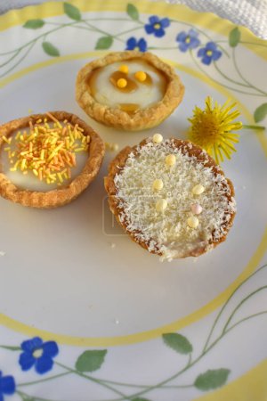 Mini tarts filled with buttercream on a  beautiful plate decorated by dandelion flower, top view