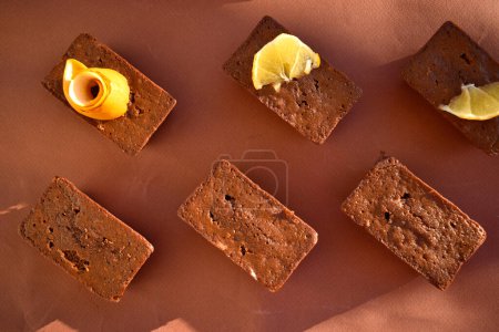 Foto de Magdalenas de chocolate decoradas con rodajas y limones sobre un fondo marrón, vista superior - Imagen libre de derechos