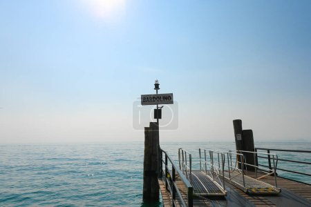 Landing bridge in Bardolino, Lake Garda, Italy, where the tourist ferries board and onboard passengers. It is a beautiful sunny summer day, with a bit of fog over the lake