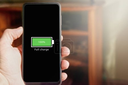 Photo for Close up of male hand holding smartphone with full battery icon on the screen indicating that battery level is at one hundred percent. Full charged battery level. - Royalty Free Image