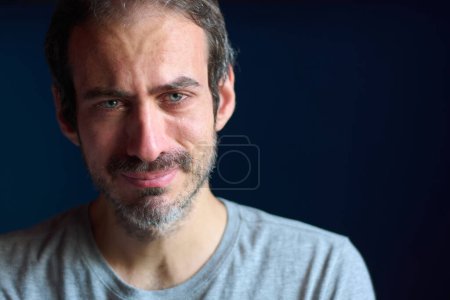 Foto de Primer plano de un joven caucásico de 30 años con barba corta y ojos azules llorando mientras mira a la cámara. Concepto de depresión, pérdida y dolor. Trauma emocional. - Imagen libre de derechos