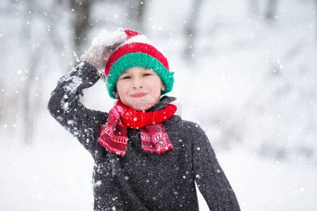 Photo for Funny little boy in winter clothes walks during a snowfall. Winter outdoor activities for children. A cute child in a warm hat rejoices at the first snow. - Royalty Free Image