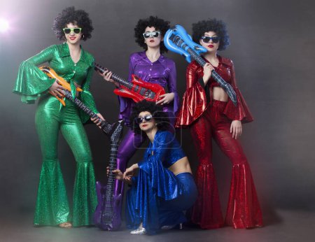 Photo for Girls in bright shiny costumes and wigs with guitars. Vintage music disco band for women in disco style. - Royalty Free Image