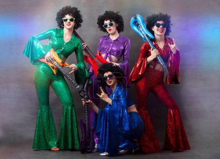 Girls in colorful shiny costumes and African wigs with guitars. Vintage music disco band for women.
