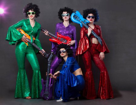 Photo for A pop music group sings in a nightclub. Young girls dressed in retro seventies costumes and funny afro wigs pose together. - Royalty Free Image