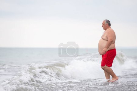 Téléchargez les photos : Un homme âgé en surpoids se repose sur la mer. - en image libre de droit