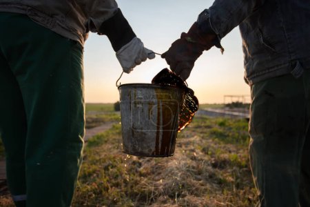 Workers carry a bucket of spilled extracted oil. Discover oil fields. Black gold.