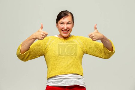 Mujer de mediana edad sonriendo mostrando signo de clase sobre fondo gris