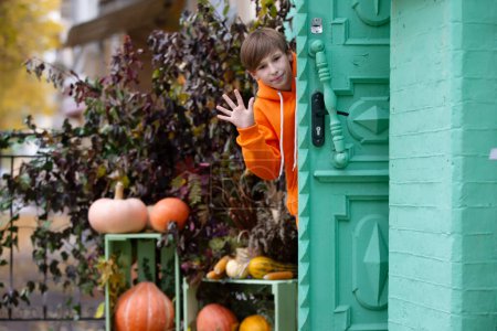 Ein Junge in orangefarbener Kleidung blickt aus der Tür eines Hauses, das zu Halloween mit Kürbissen dekoriert ist.