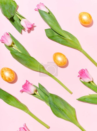 Foto de Flatlay with a pattern of golden easter eggs and tulips on pink background - Imagen libre de derechos