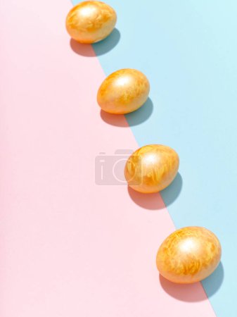 Foto de Diseño creativo con huevos de Pascua dorados de colores sobre fondo azul brillante y rosa. Concepto de imágenes festivas - Imagen libre de derechos