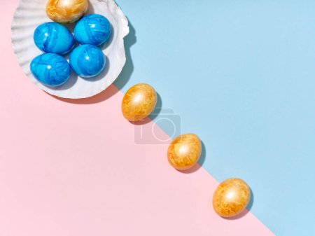 Foto de Diseño creativo con huevos de Pascua de colores dispuestos en una concha sobre fondo azul brillante y rosa. Una plantilla para contenido festivo - Imagen libre de derechos