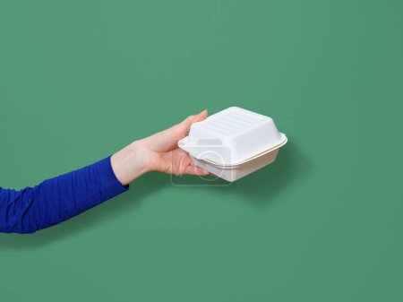 Téléchargez les photos : Main féminine tenant le récipient de nourriture pour burger à emporter sur fond vert. Lumière flash, espace de copie - en image libre de droit