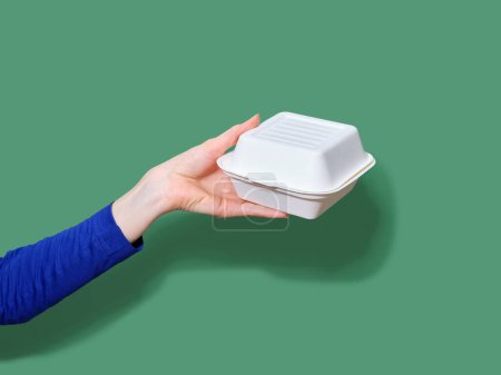 Photo for Female hand holding food container for takeaway burger on green background. Flash light, copy space - Royalty Free Image