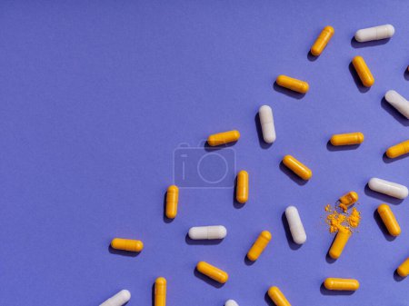 Foto de Pastillas de vitaminas naranja y blanca sobre fondo violeta - Imagen libre de derechos