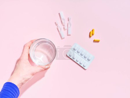 Foto de Composición creativa con píldoras de suplemento alimenticio, vaso de agua y mano femenina sobre fondo colorido - Imagen libre de derechos