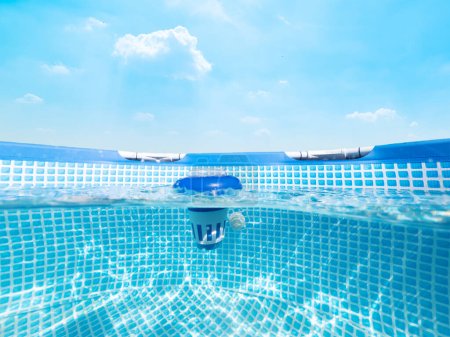 Vista submarina dividida de un dispensador de cloro flotante en una piscina bajo un cielo azul
