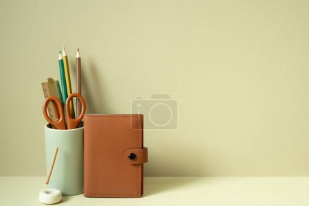Foto de Cuaderno y artículos de escritura portalápices en el escritorio. fondo beige caqui - Imagen libre de derechos