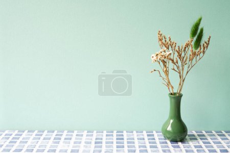 Grüne Vase mit trockener Blume auf blauem Fliesentisch. Mint Wall Hintergrund