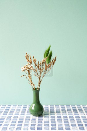 Green vase of dry flower on blue tile table. mint wall background