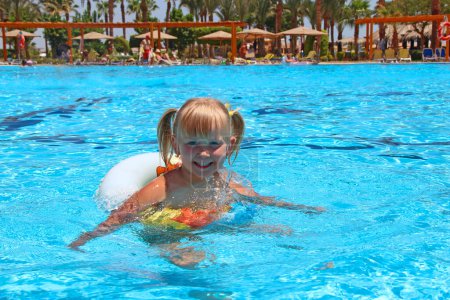 Photo for Smiling baby girl with nice plaits swimming in swimming pool lying on inflatable circle on summer holidays. Happy childhood. Child relaxing on rubber circle on blue water of pool during holidays - Royalty Free Image