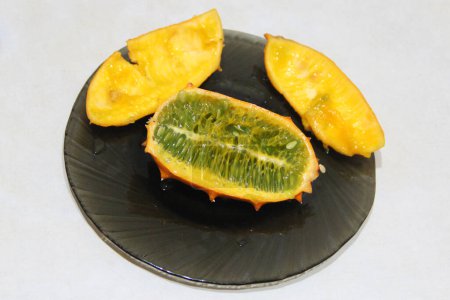 Cortar la fruta kiwano en el plato. Fruto maduro de Cucumis metuliferus. Comió fruta kiwano en un plato. Pepino de cuernos africano amarillo. Melón de jalea maduro