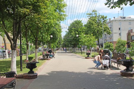 Photo for Gomel - Belarus - May 20, 2018 : Street of Belarusian city of Gomel with benches trees and hanging garlands. People resting in park with benches and garlands. People relax in city. Beautiful city park. Place for rest - Royalty Free Image