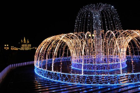 Photo for Beautiful fountain of colored holiday garlands glittering and flashing in city park in winter. Christmas and New Year's winter holiday lights. City panorama with fontains made from garlands - Royalty Free Image