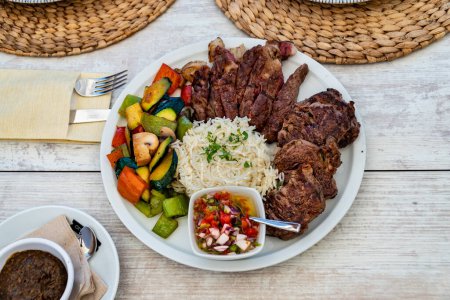 a view over a plate of grilled meat served with rice and mixed vegetables at a restaurant.