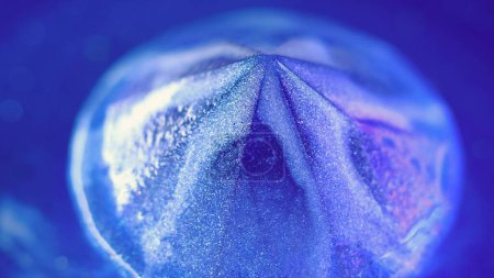 Sparkling diamond. Shimmer crystal. Glitter paint. Defocused blue purple color neon iridescent luminous gemstone shiny glossy liquid reflected rainbow light abstract art background.