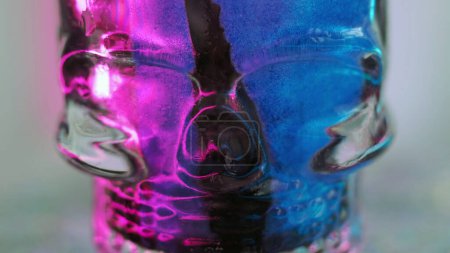 Skull glass. Paint flow. Neon ink. Defocused blue purple pink black color luminous drip glitter liquid spilling on dark dummy with disco light abstract art background.
