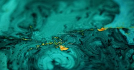 Ink spill. Glitter fluid mix. Defocused cyan blue green black golden color glowing sparkling marble texture acrylic wave abstract art background.